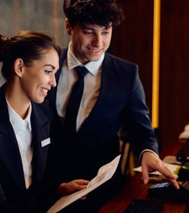 Happy hotel managers through reservation list on desktop PC at reception desk. Happy hotel managers through reservation list on desktop PC at reception desk.
